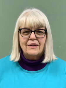A woman with white hair wearing glasses and blue shirt.