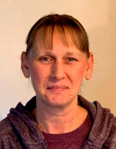 A woman with brown hair and bangs wearing a purple shirt.